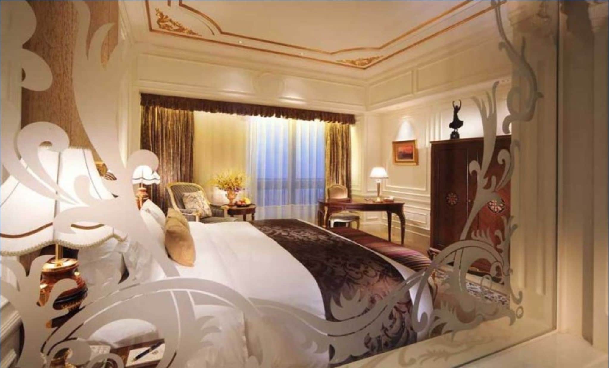 A luxurious hotel room with a large bed, ornate curtains, a desk, and a chair.