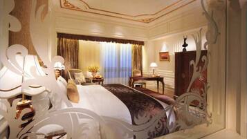A luxurious hotel room with a large bed, ornate curtains, a desk, and a chair.