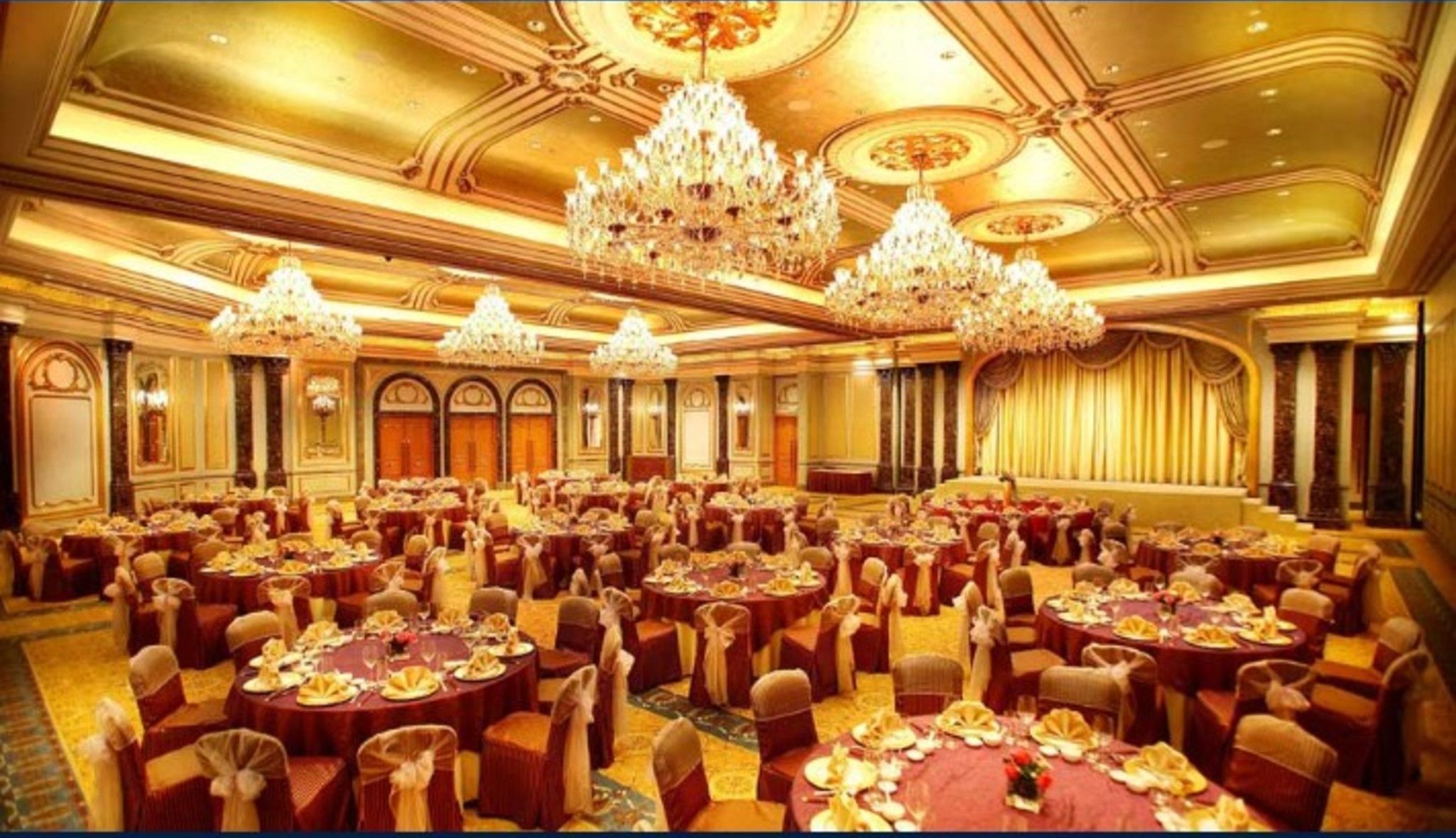 A large banquet hall with round tables, chandeliers, and ornate ceiling details.