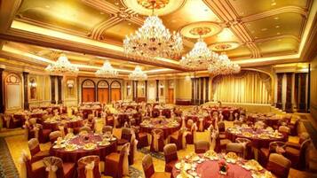 A large banquet hall with round tables, chandeliers, and ornate ceiling details.