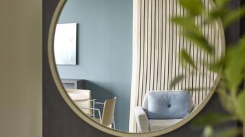 A room with a circular mirror reflecting a bed, a chair, and a wall-mounted TV.