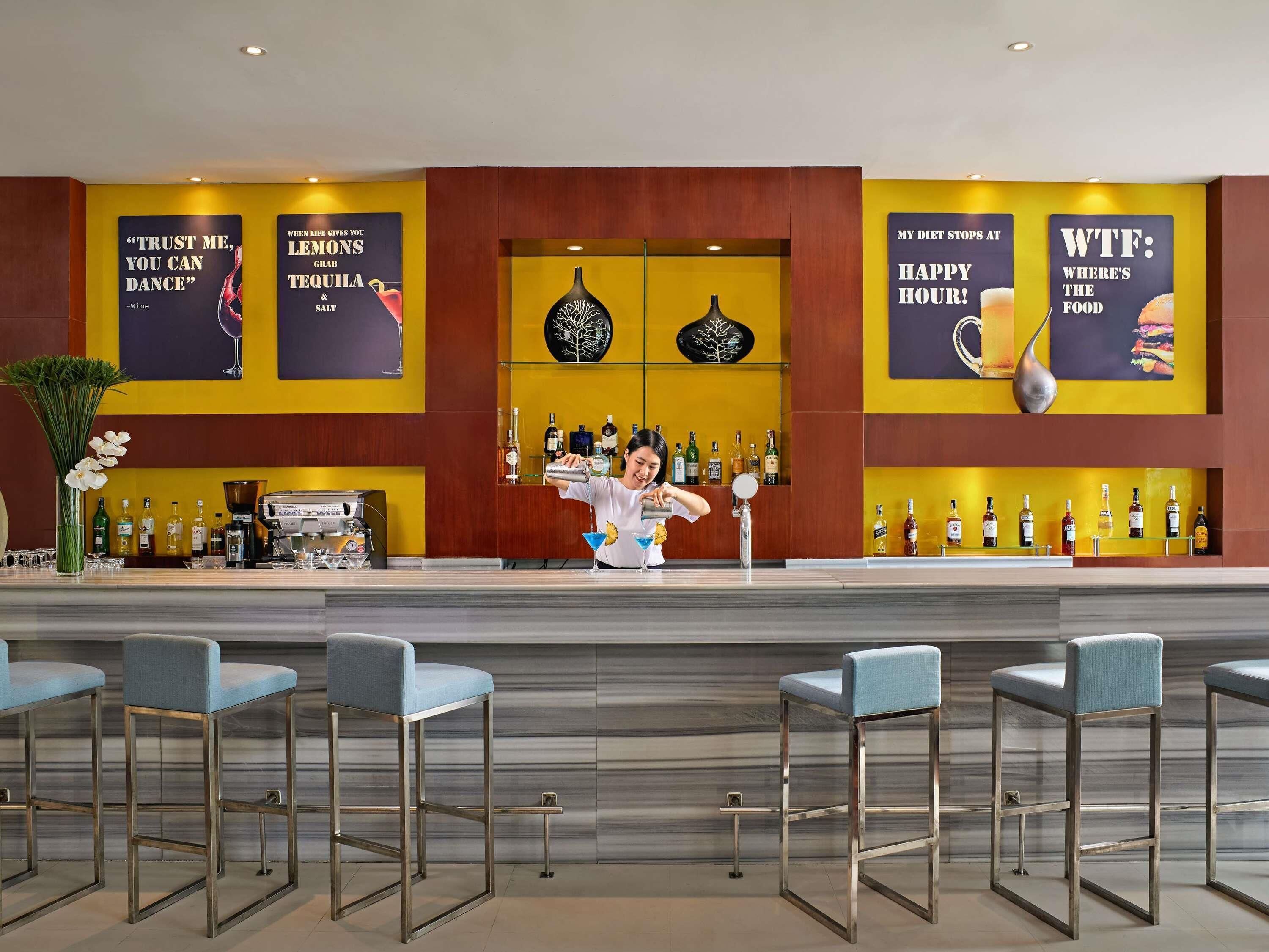 A bar area with a bartender preparing drinks, bar stools, and a variety of bottles and glasses on shelves.