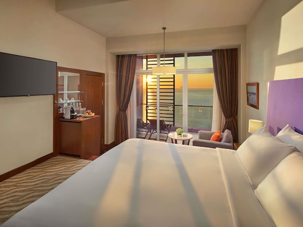 A hotel room with a bed, a desk with a coffee machine, a small table, and a balcony with a view of the sea.
