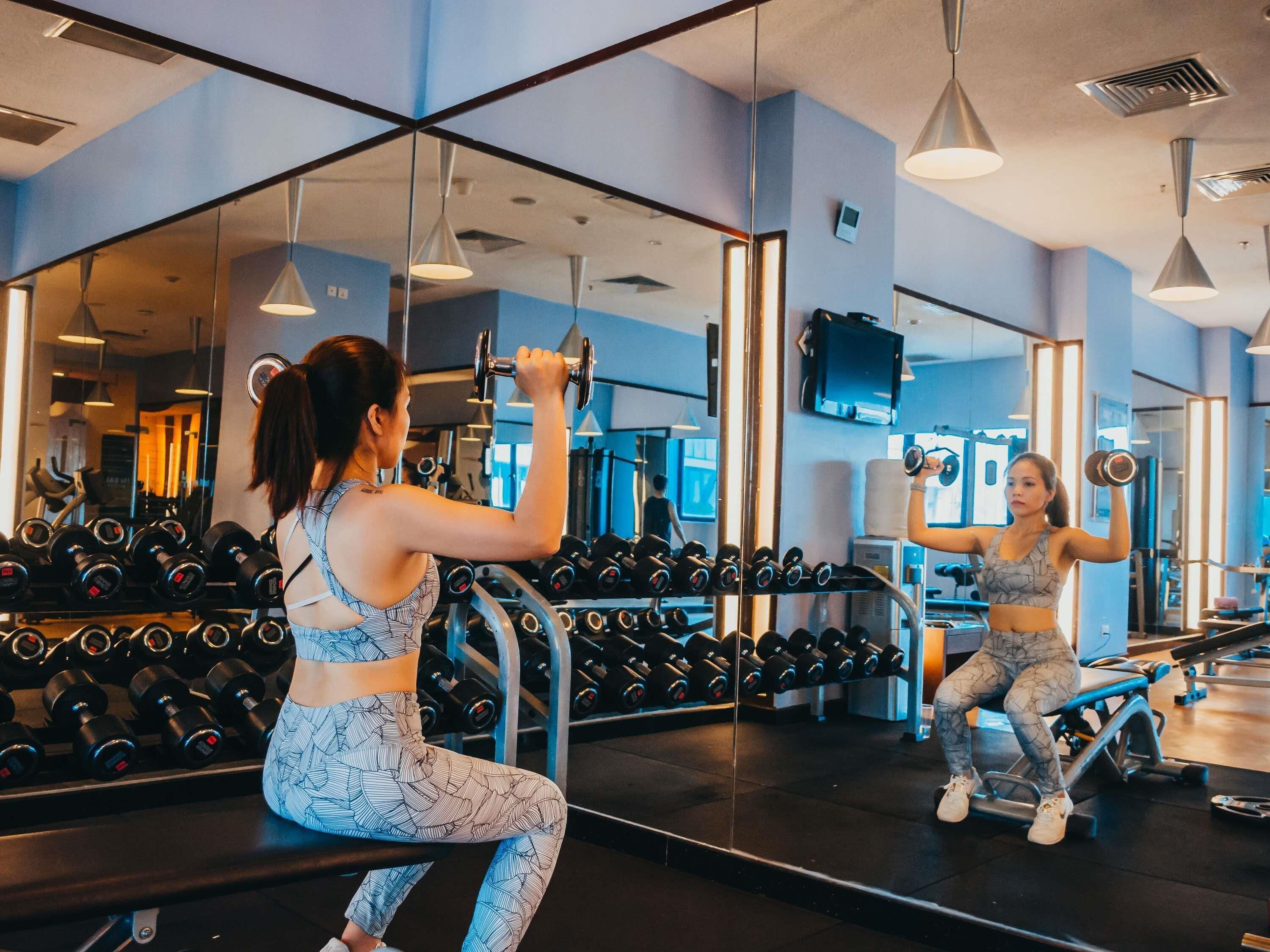 Een sportschool met trainingsapparatuur, spiegels en een televisie aan de muur.