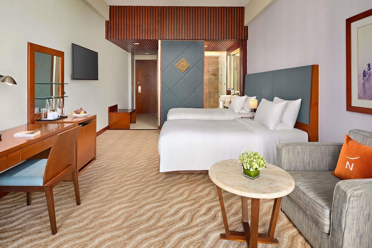 A hotel room with a bed, a desk, a chair, a sofa, a small table, and a mirror.