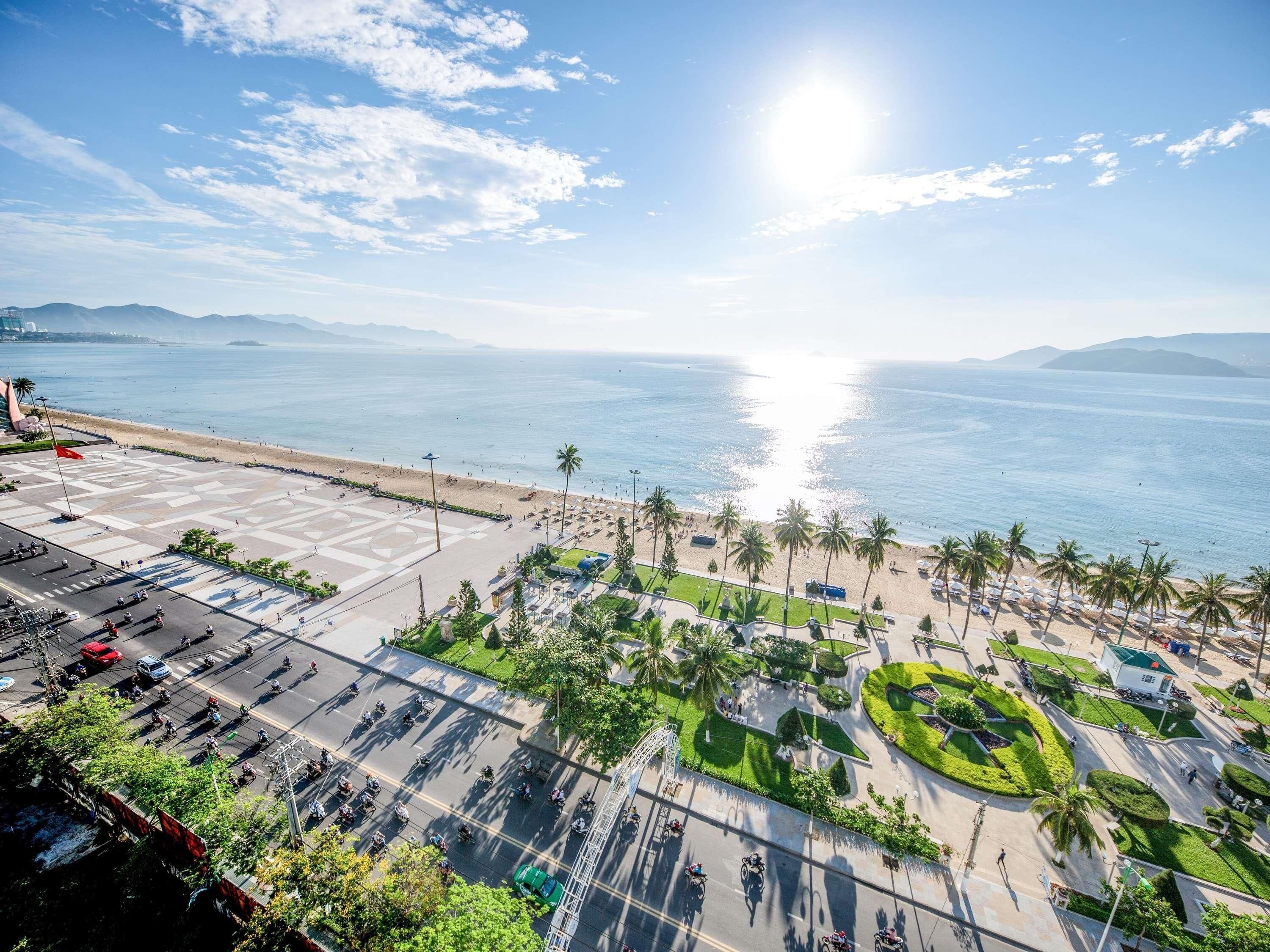 Μια αεροφωτογραφία μιας παράκτιας περιοχής με μια παραλία, φοίνικες και έναν χώρο στάθμευσης.