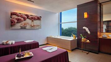 Relax in a serene spa room with two massage tables, a large window offering a view of the outdoors, and a beautiful painting of roses.