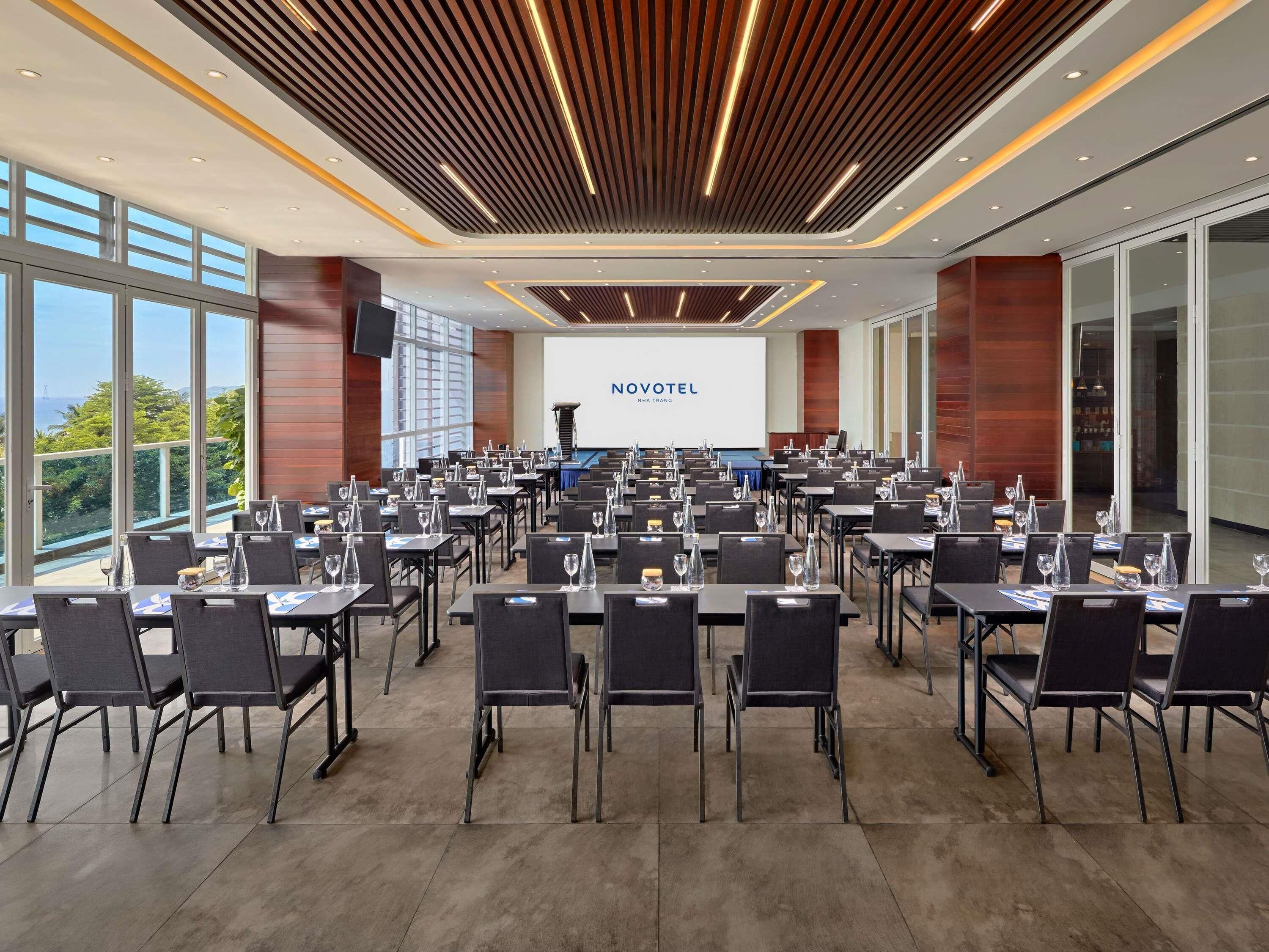 A conference room with tables and chairs, a presentation screen, and a view of the outdoors.