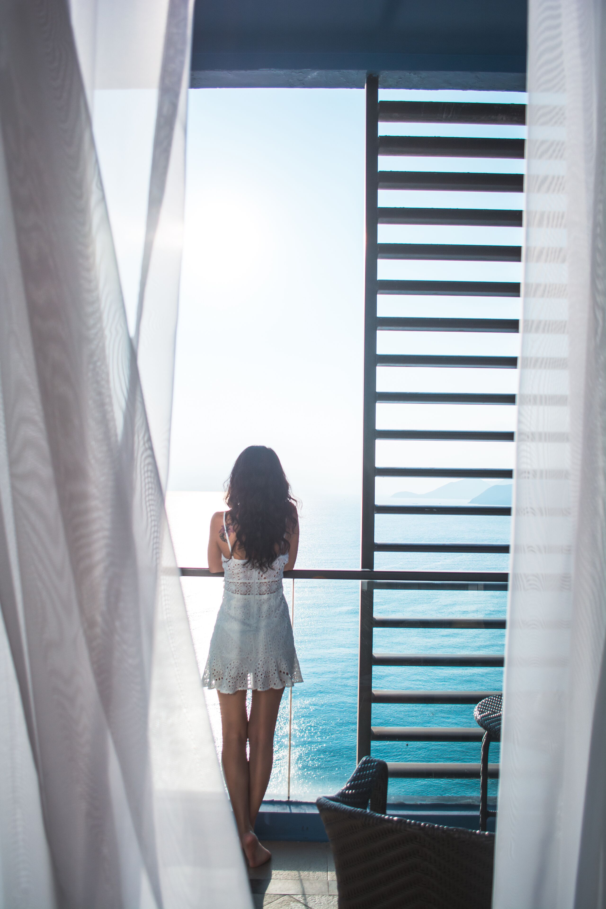 Un balcón con vistas al mar, una silla de mimbre y una persona de pie.