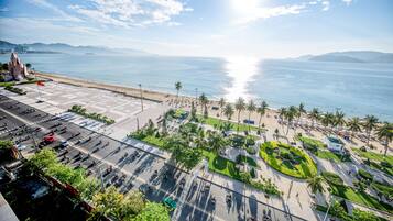 A coastal cityscape with a wide boulevard, palm trees, and a beach in the background.