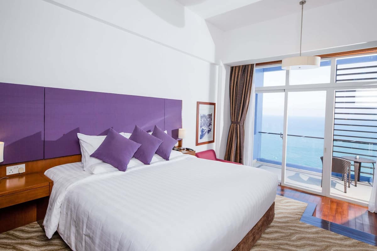 A hotel room with a large bed, a view of the sea, and a balcony with outdoor furniture.
