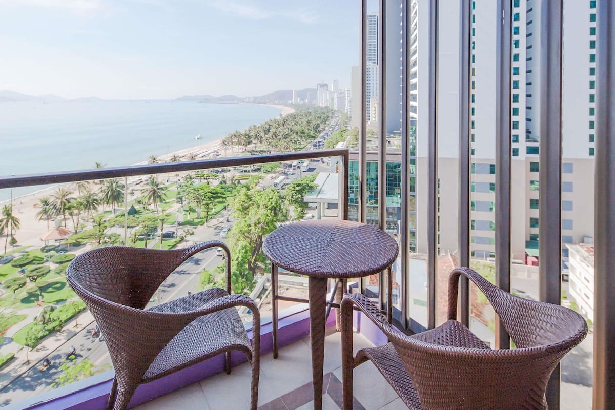 A balcony with wicker furniture overlooking a beach and cityscape.