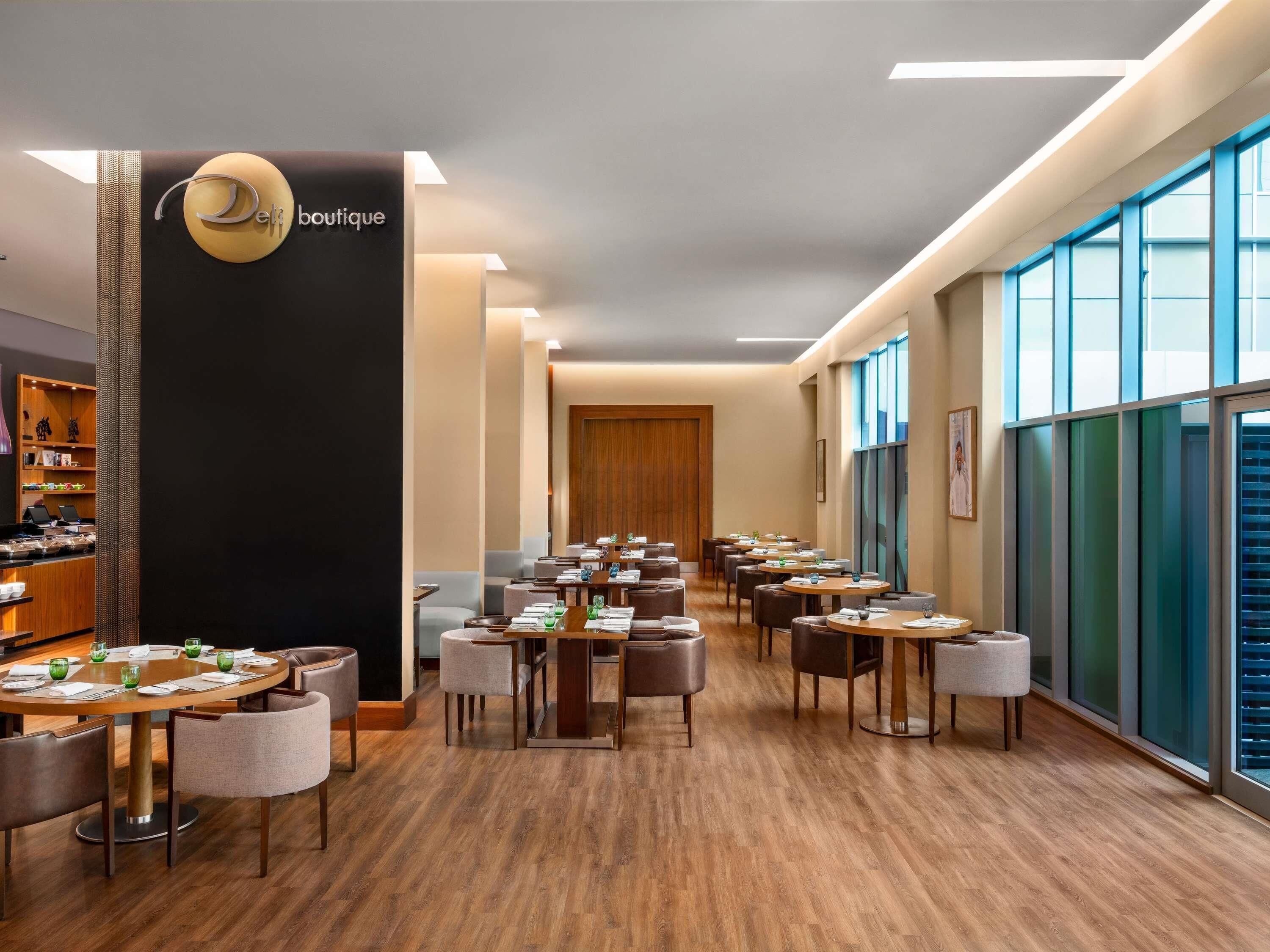 A modern hotel lobby with a reception desk, a seating area with round tables and chairs, and large windows offering views.