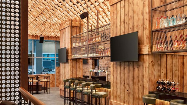 Un espace bar avec des murs en bois, un téléviseur fixé au mur et un comptoir de bar avec des tabourets.