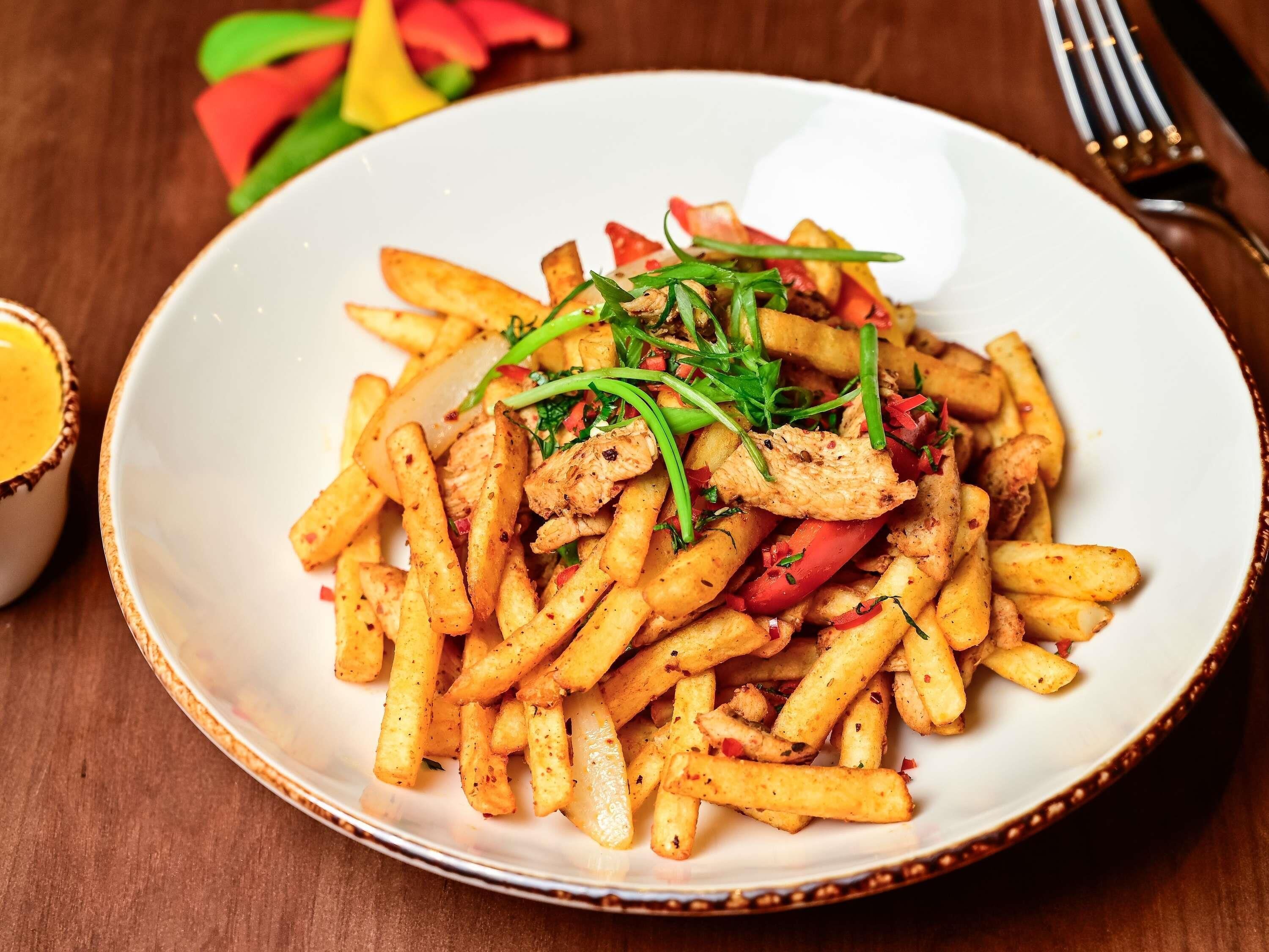 A plate of seasoned fries with chicken and vegetables.