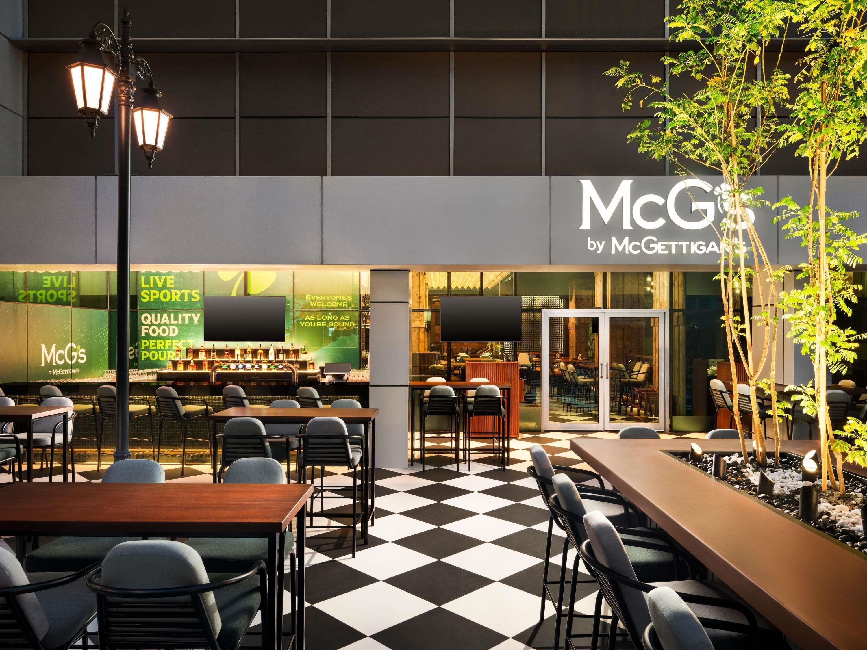 Un área de estar al aire libre con mesas y sillas, un bar con un fondo verde y un letrero de McGettigan's.