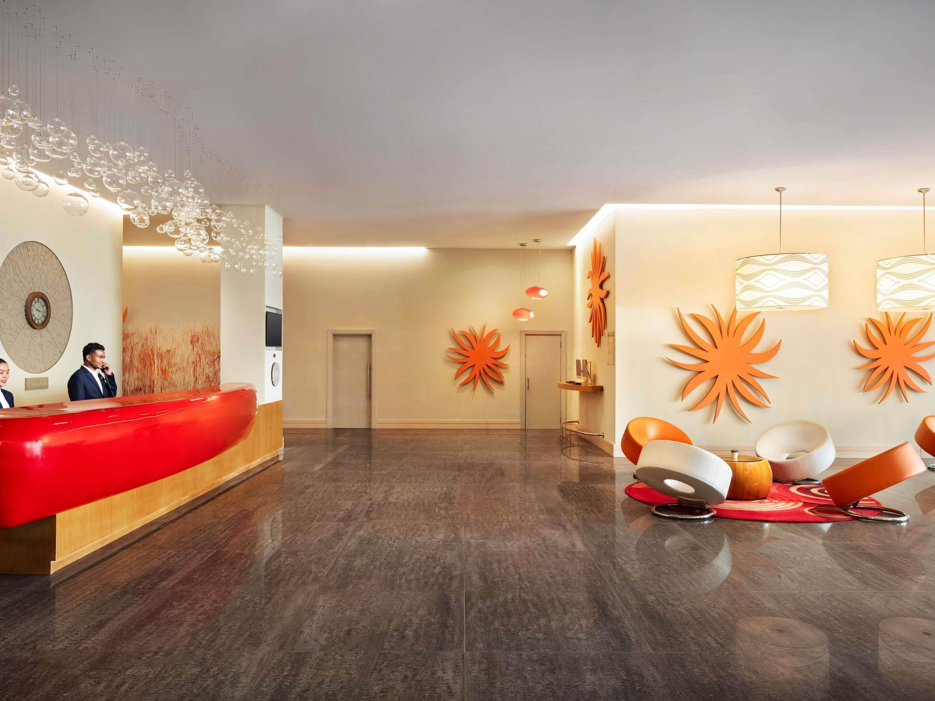 A modern hotel lobby with a reception desk, a waiting area with chairs, and decorative wall art.