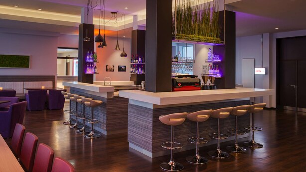 Zona de bar moderna con una barra central, varios taburetes y una amplia selección de botellas y vasos.