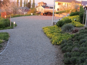 Un camino de grava que conduce a una casa con porche cubierto, rodeada de jardines ajardinados y una cerca.