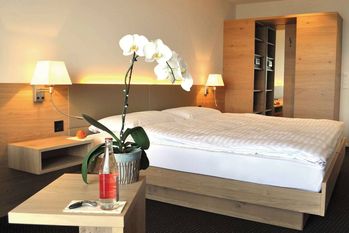 Habitació d'hotel amb un llit, dues taules de nit i una orquídia en test, juntament amb una ampolla d'aigua.