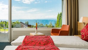 Habitación de hotel con un ventanal que ofrece vistas al mar y follaje.