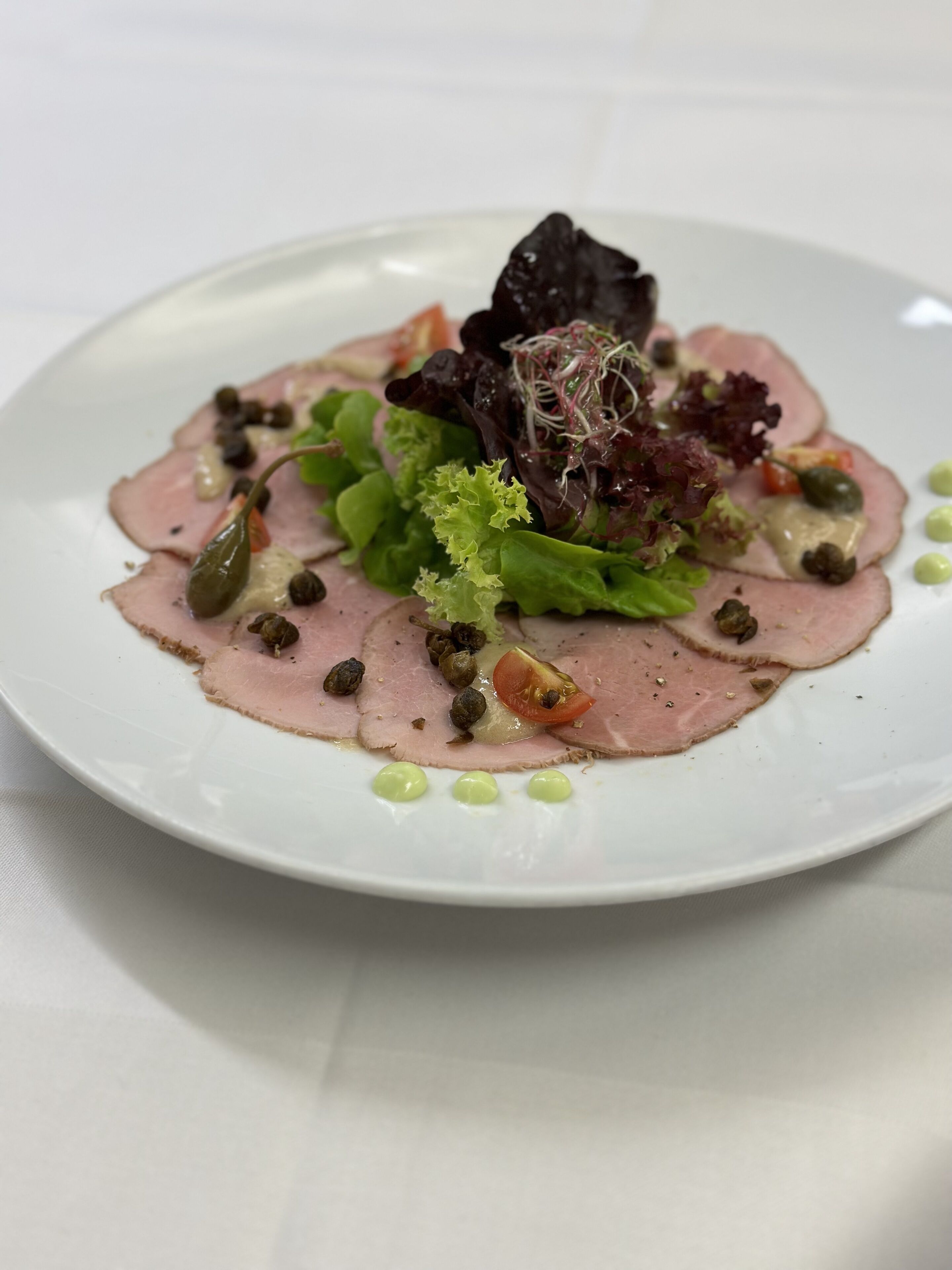 Ein Teller Essen mit Fleischscheiben, Grünzeug und Kapern.