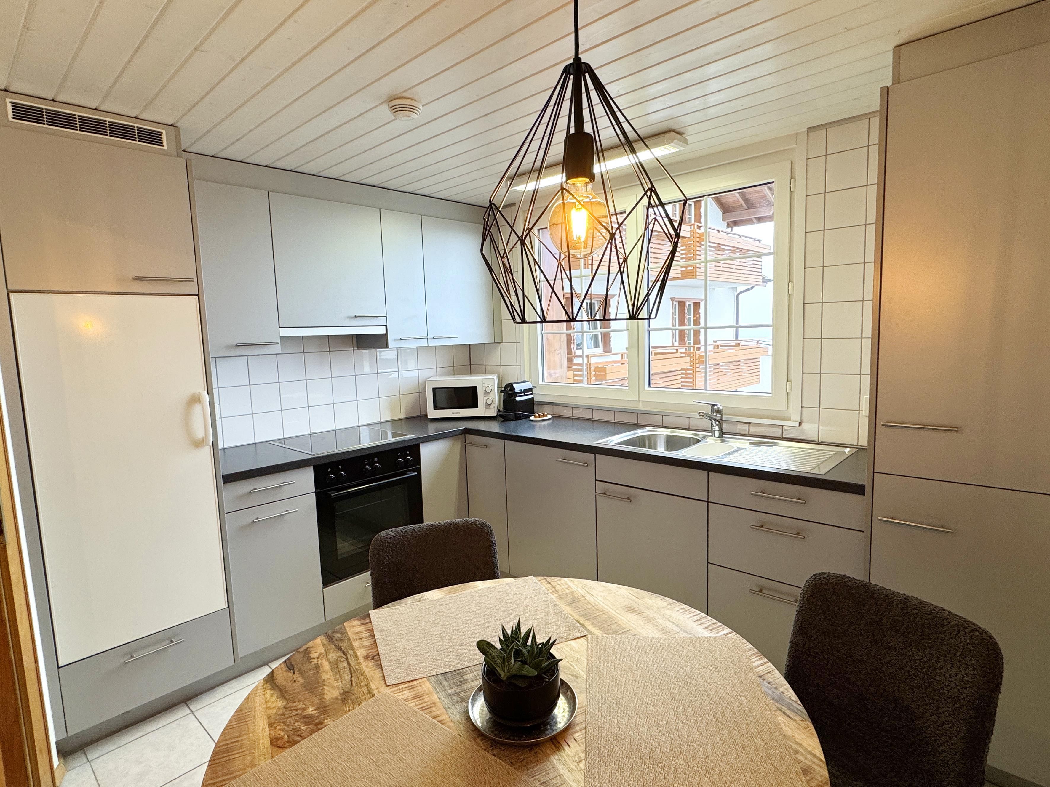 A modern kitchen with white cabinets, a microwave, a sink, and a dining table with chairs.