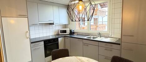A modern kitchen with white cabinets, a microwave, a sink, and a dining table with chairs.
