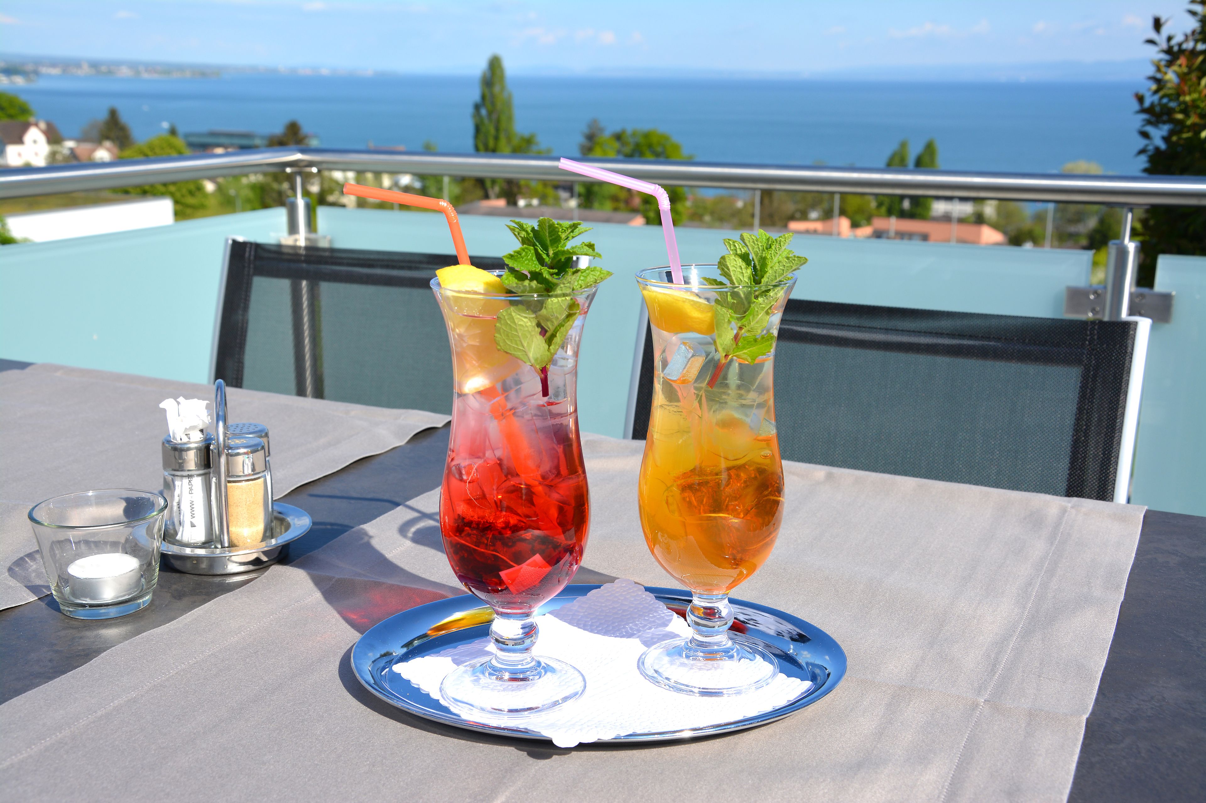 Two drinks on a tray with a scenic view of the sea in the background.