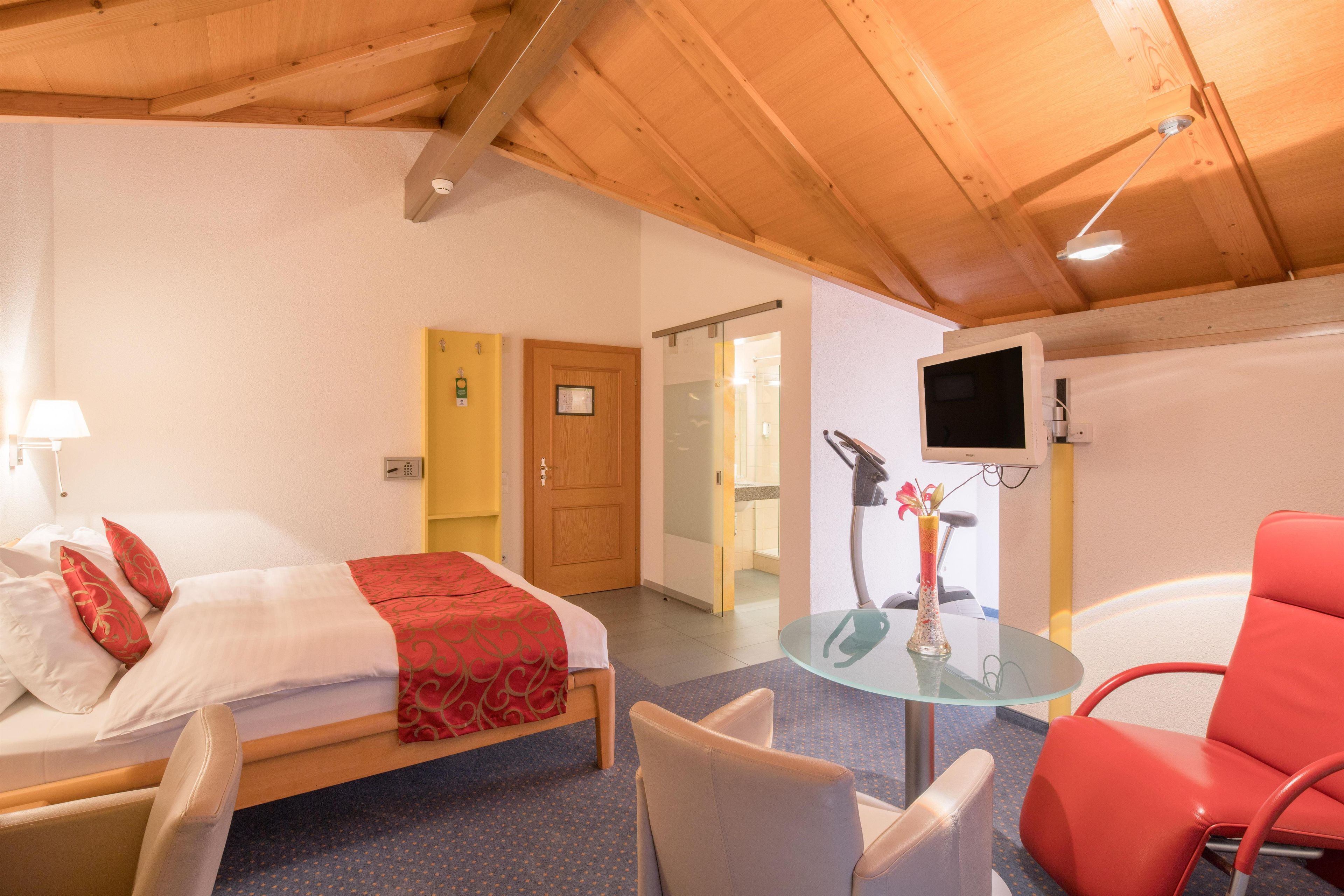 Una habitación de hotel con cama, escritorio, silla, televisor y puerta de baño.