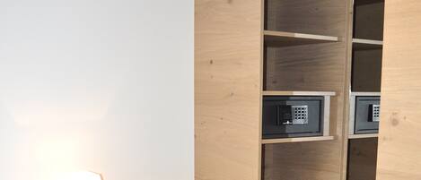 A hotel room with a wooden wardrobe, a bedside table with a lamp, and a black carpet with a dotted pattern.