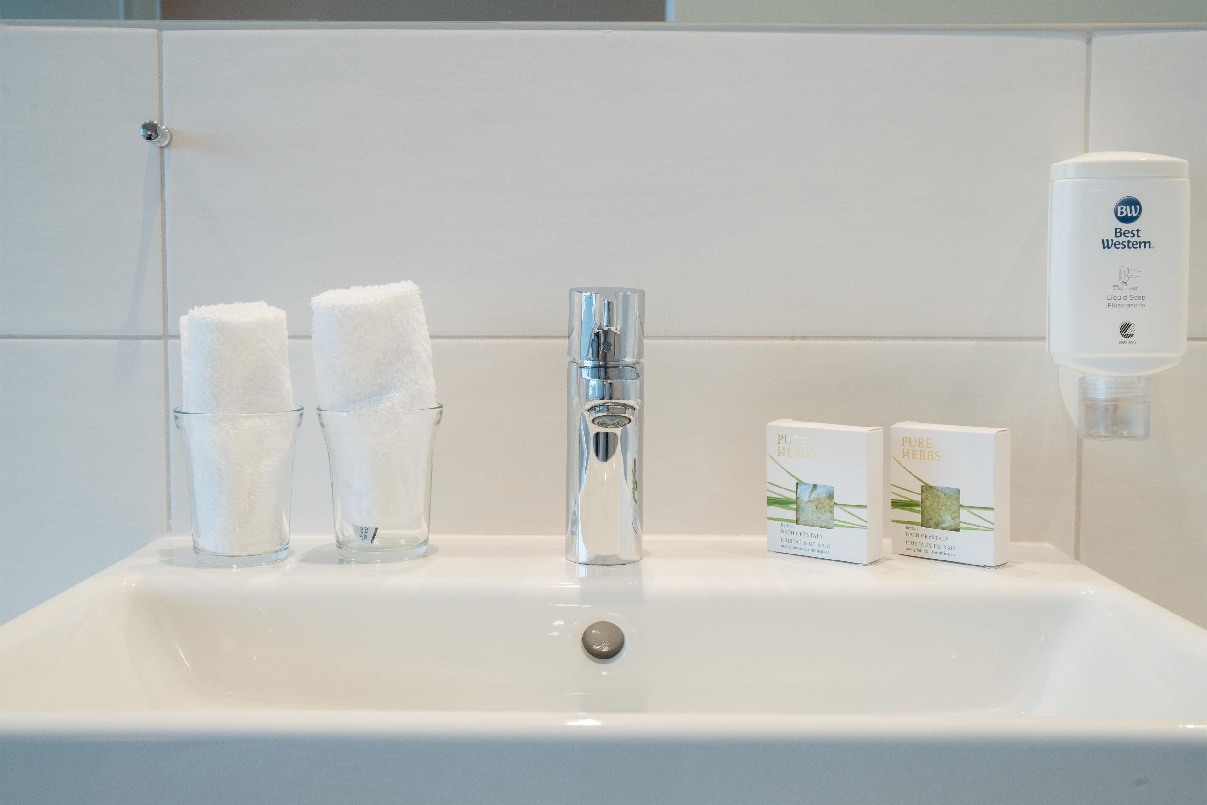 Un lavabo de salle de bain avec deux récipients en verre, un robinet et deux boîtes de sels de bain.