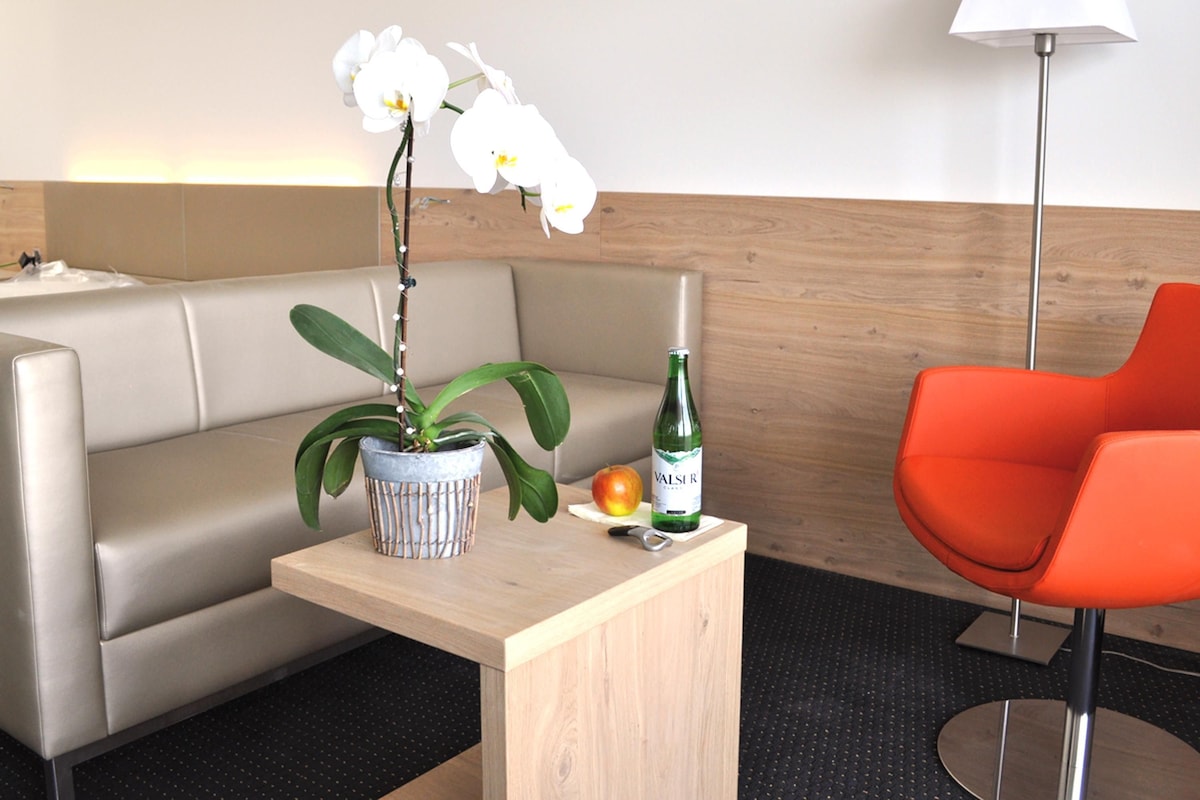A hotel room with a sofa, a small table with a potted plant, a bottle, and an apple.