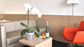 Et hotelværelse med en sofa, et lille bord med en potteplante, en flaske og et æble.