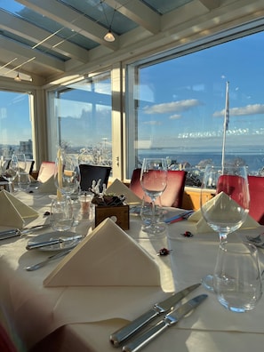 Mesa de comedor dispuesta con cristalería, cubiertos y una vela, con vistas a un paisaje panorámico.