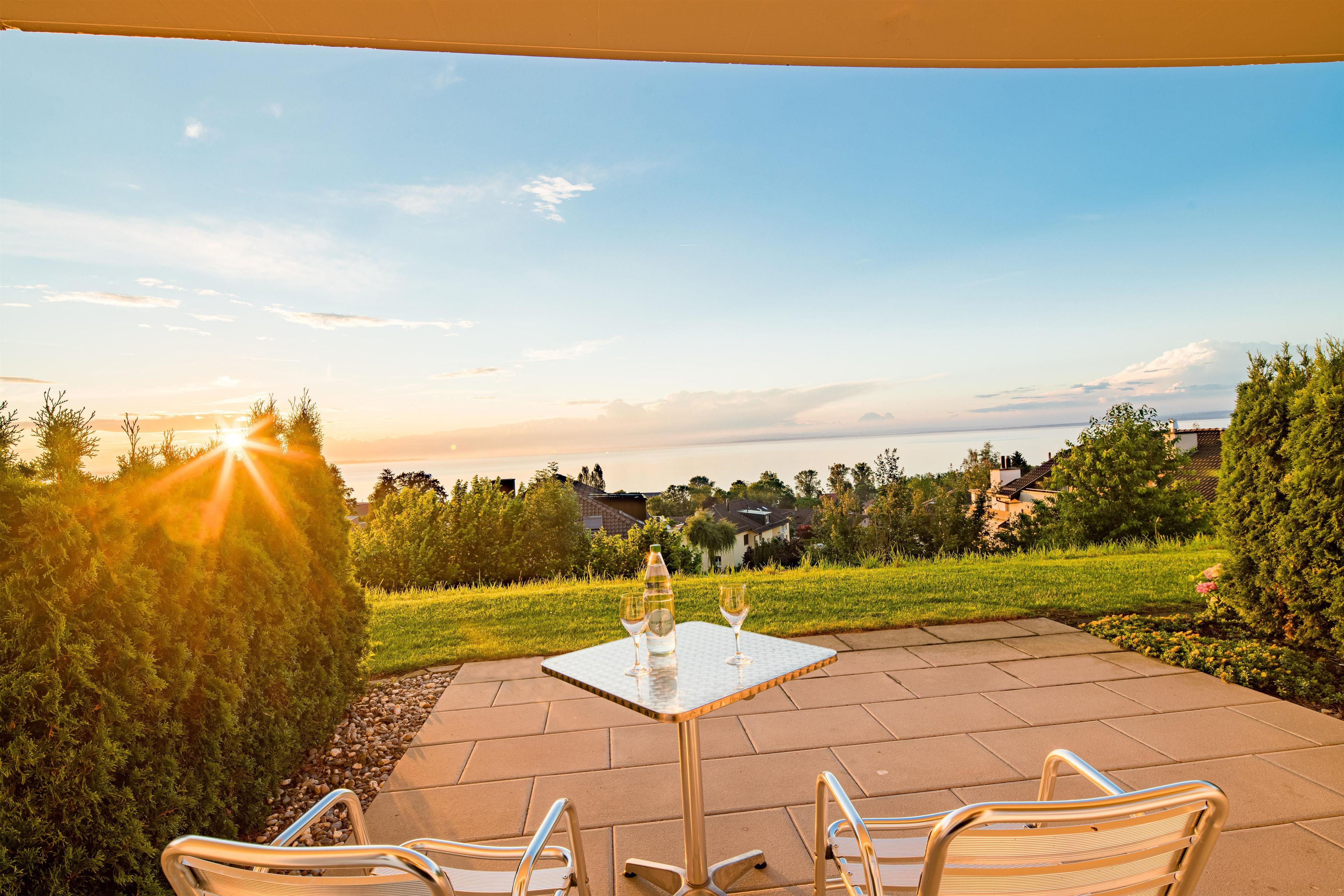 An outdoor patio with a table and chairs, a bottle of wine, and a glass.