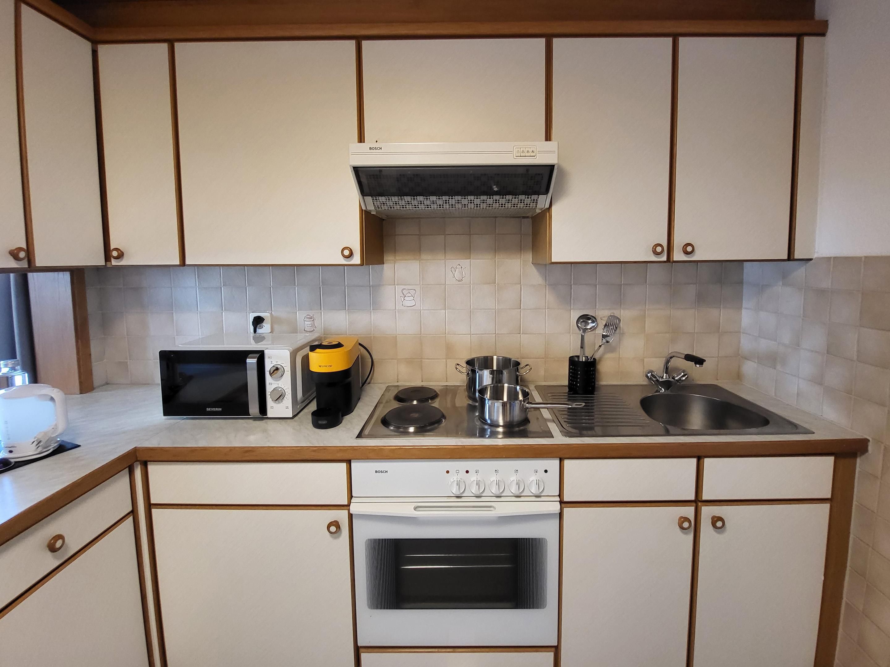 Een keuken met een Bosch magnetron, koffiezetapparaat, waterkoker en oven.