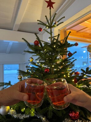 A decorated Christmas tree with ornaments and lights, and two hands holding glasses of red liquid.
