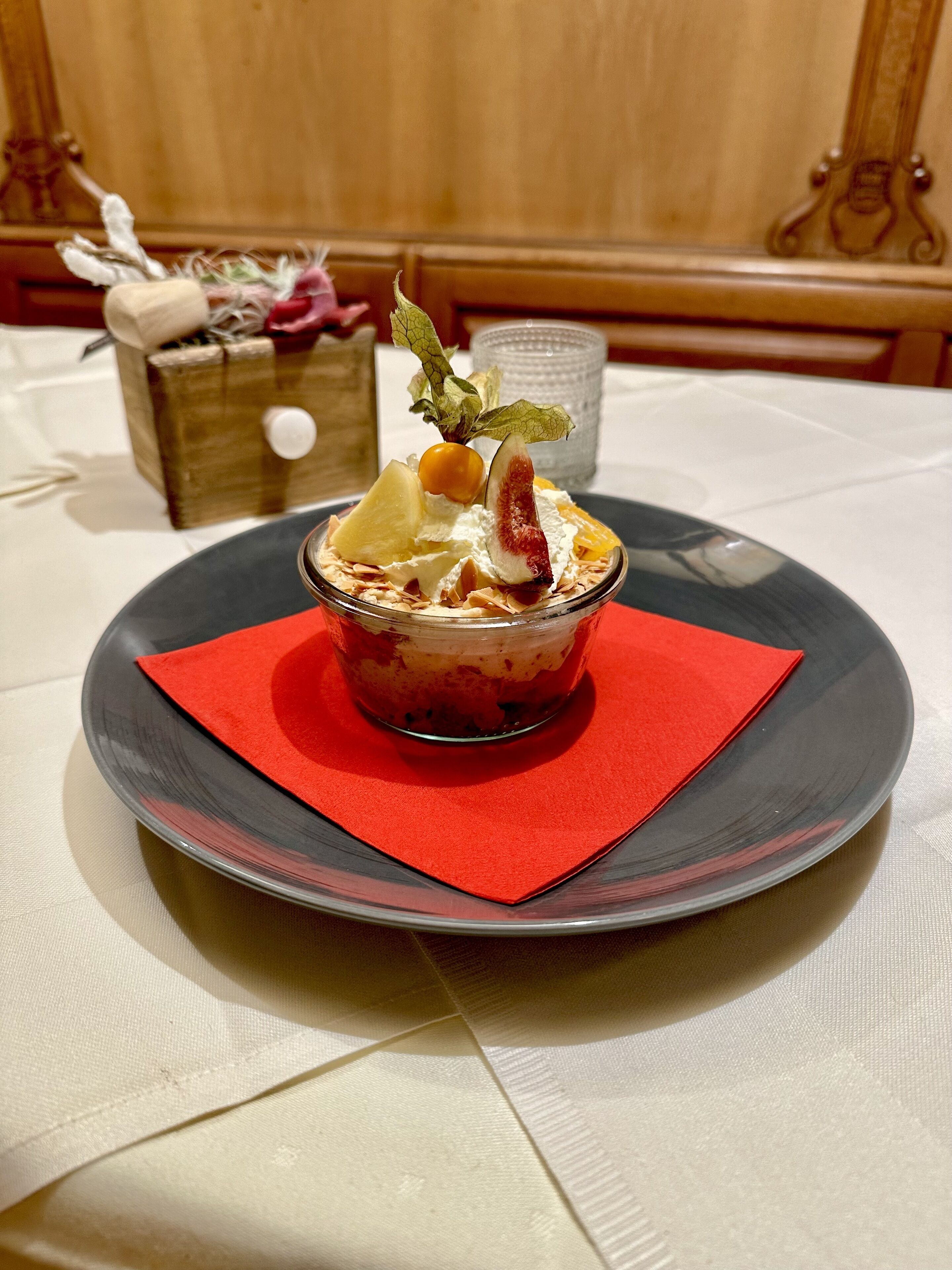 Un dessert présenté sur une assiette, accompagné d’une serviette rouge, d’un verre d’eau et d’une boîte en bois en arrière-plan.