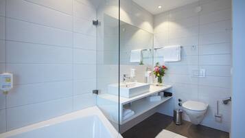 Ein modernes Badezimmer mit Duschkabine aus Glas, einer weißen Badewanne, einem Waschtisch mit Spüle und einer Toilette.
