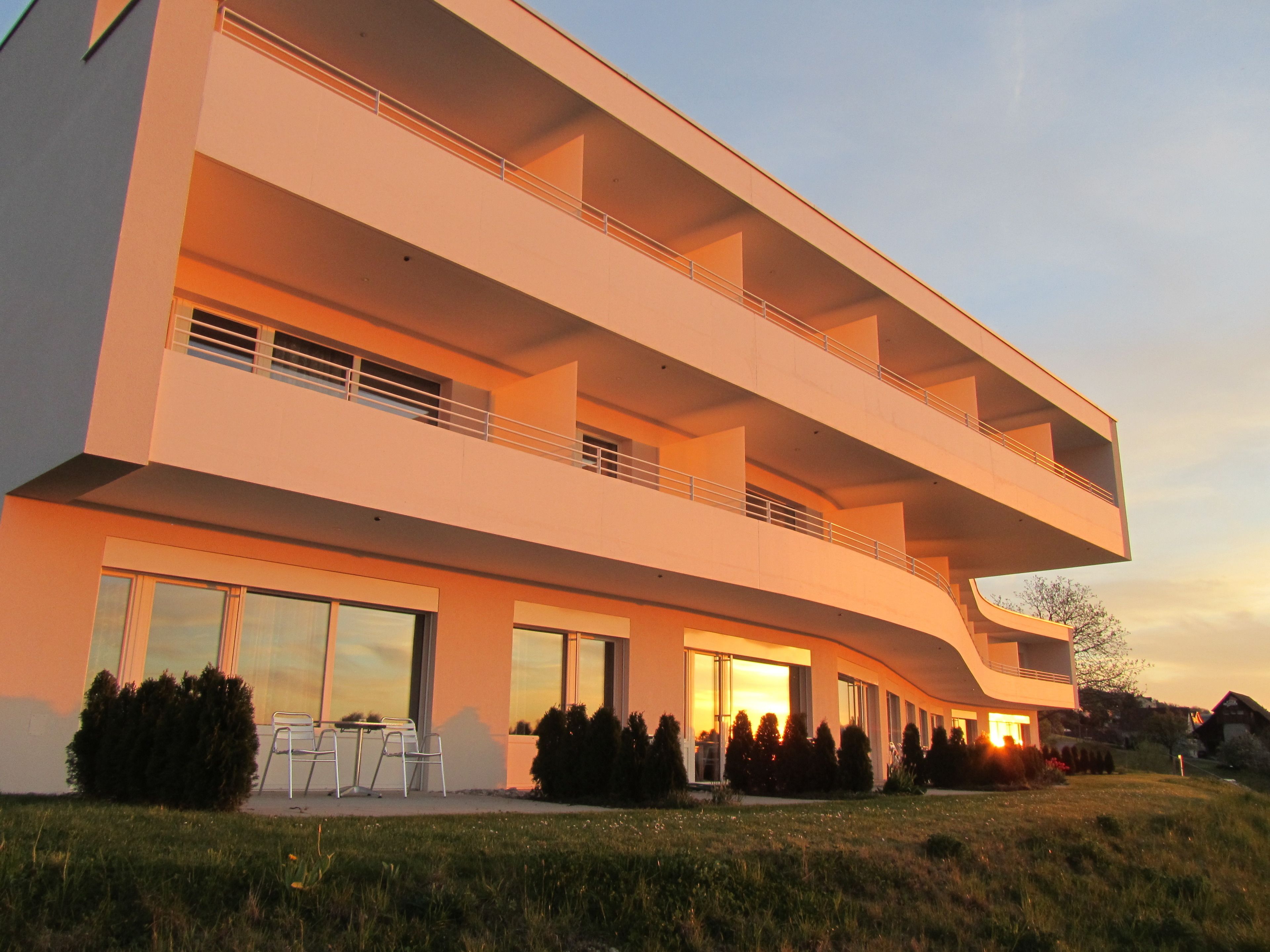 A modern multi-story building with balconies, large windows, and a well-maintained lawn.