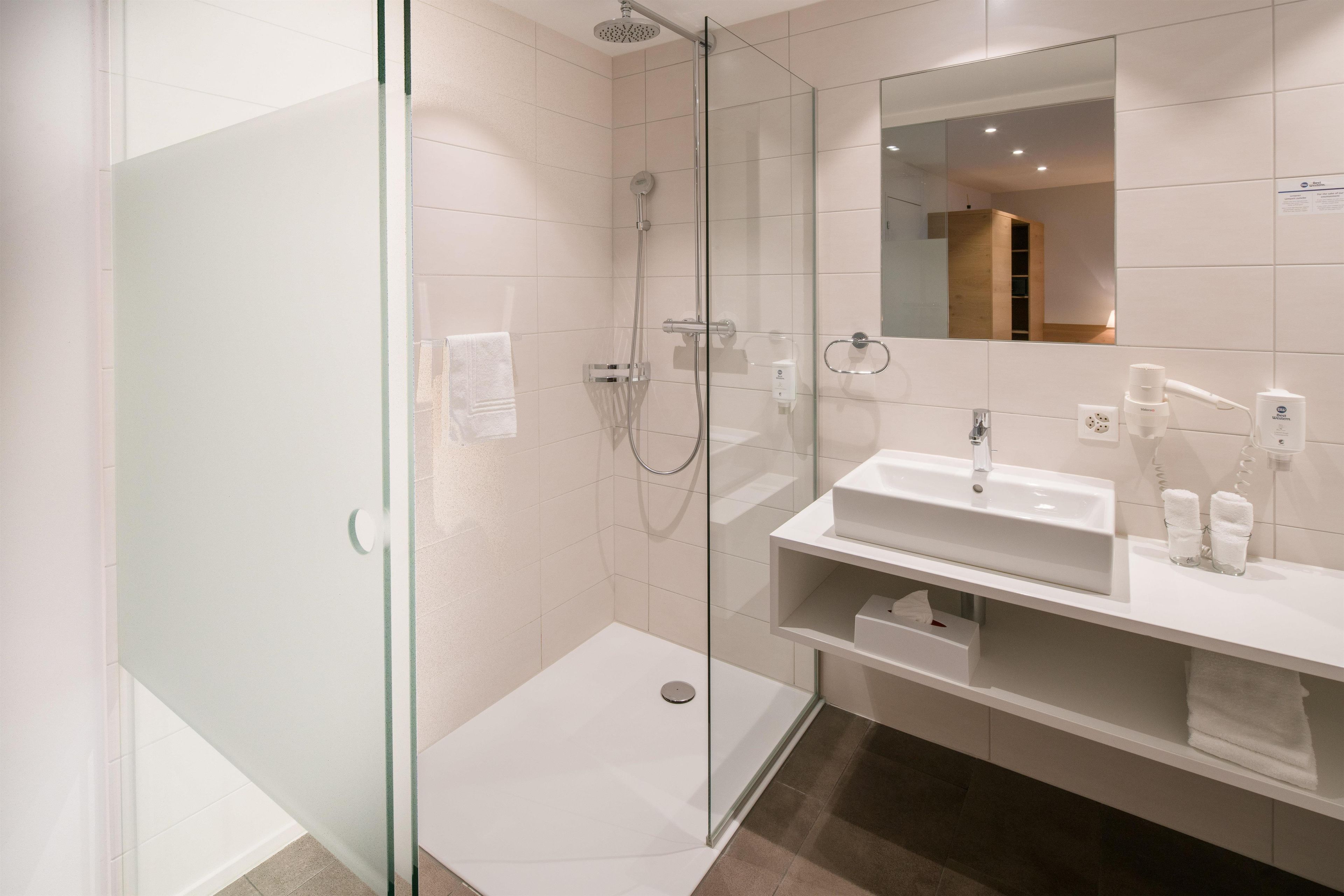 Ein modernes Badezimmer mit einer begehbaren Glasdusche, einem weißen Waschbecken und einem Spiegel über dem Waschtisch.