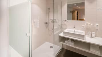Ein modernes Badezimmer mit einer begehbaren Glasdusche, einem weißen Waschbecken und einem Spiegel über dem Waschtisch.