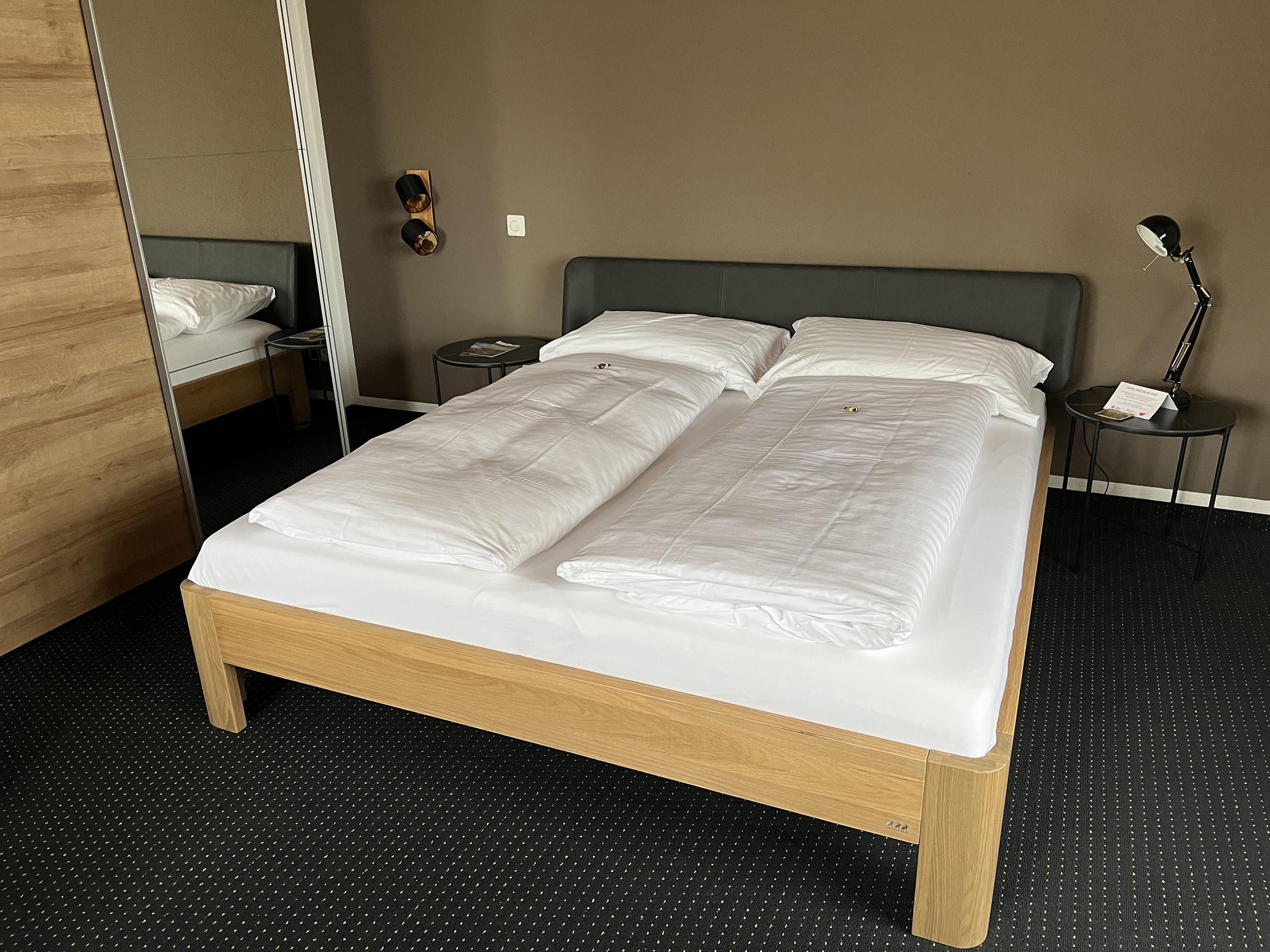 Una habitación de hotel con una cama de madera, una mesita de noche con lámpara y un espejo.