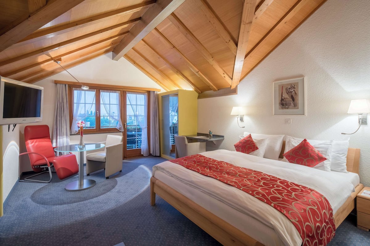 Habitació d'hotel amb un llit gran, una taula de treball, una cadira vermella i una televisió.