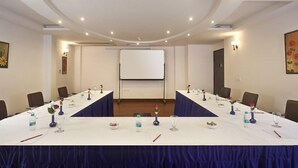 A conference room with a long table, chairs, a projector screen, and floral centerpieces. - Hotel Saptagiri (New Delhi)