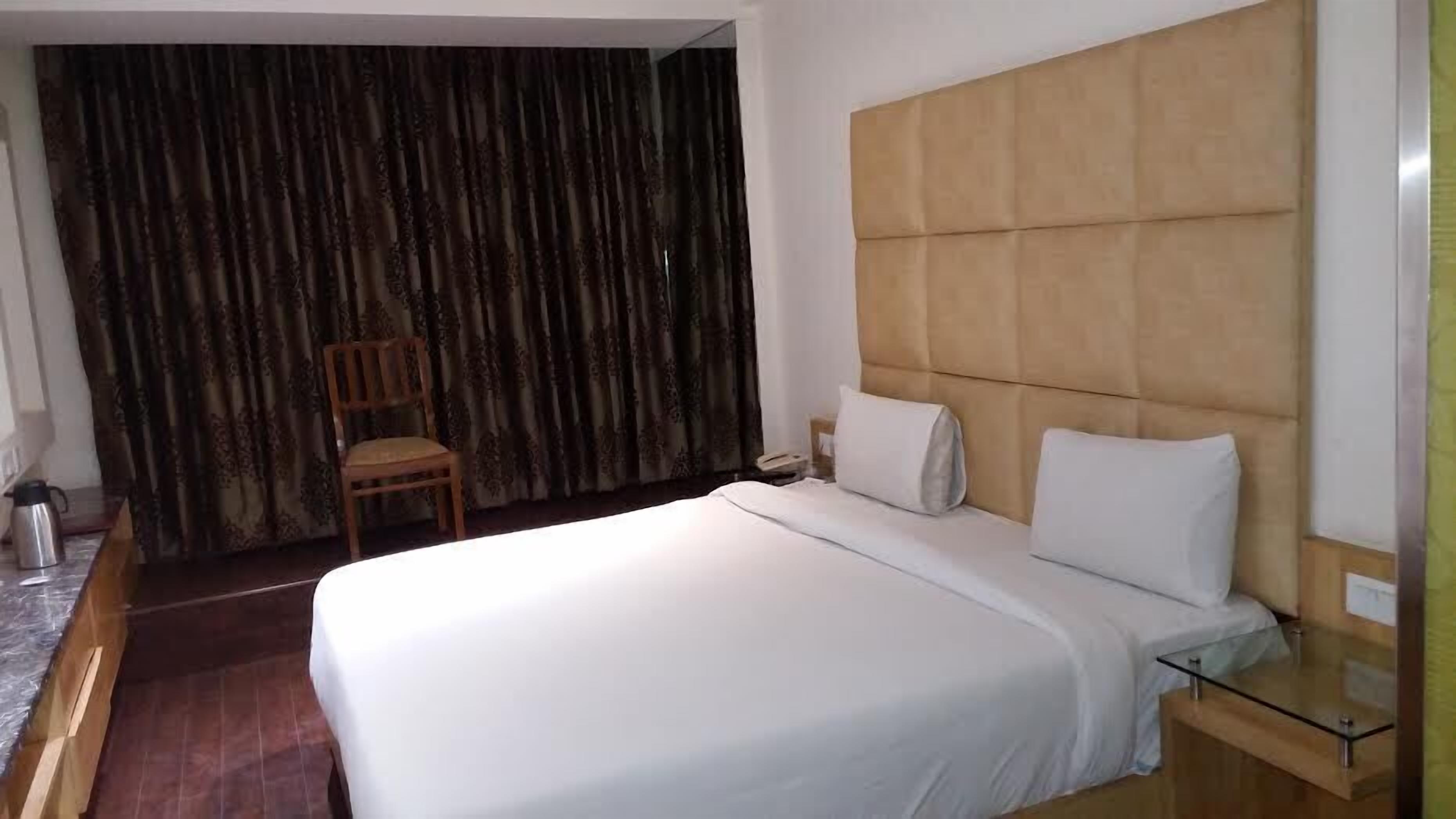 A hotel room with a large bed, a wooden headboard, a glass side table, and a chair.