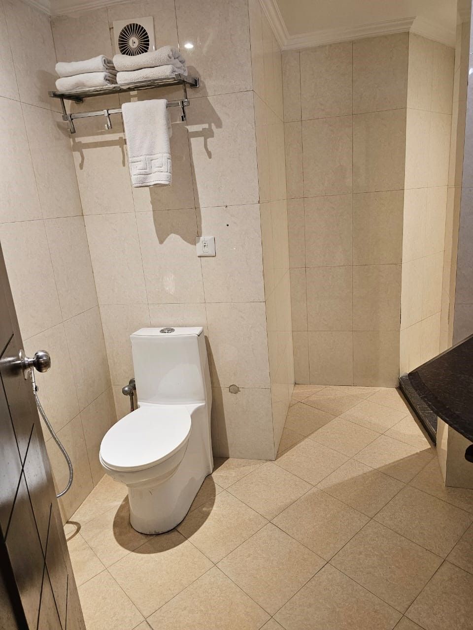 A bathroom with a toilet, a shower area, and a towel rack with folded towels.