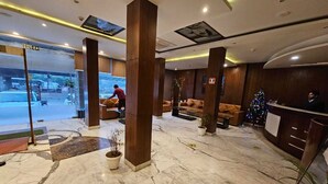 A hotel lobby with marble flooring, wooden pillars, a reception desk, and a Christmas tree. - Hotel Saptagiri (New Delhi)