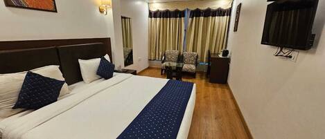A hotel room with a large bed, a desk, a chair, a TV, and a painting on the wall.